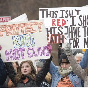 Teenage girls holding signs in a crowd that say "protect kids not guns"
